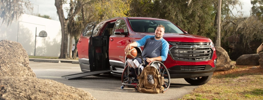 Man in manual wheelchair holding a basketball sitting next to BraunAbility Chevy Traverse with the ramp door open